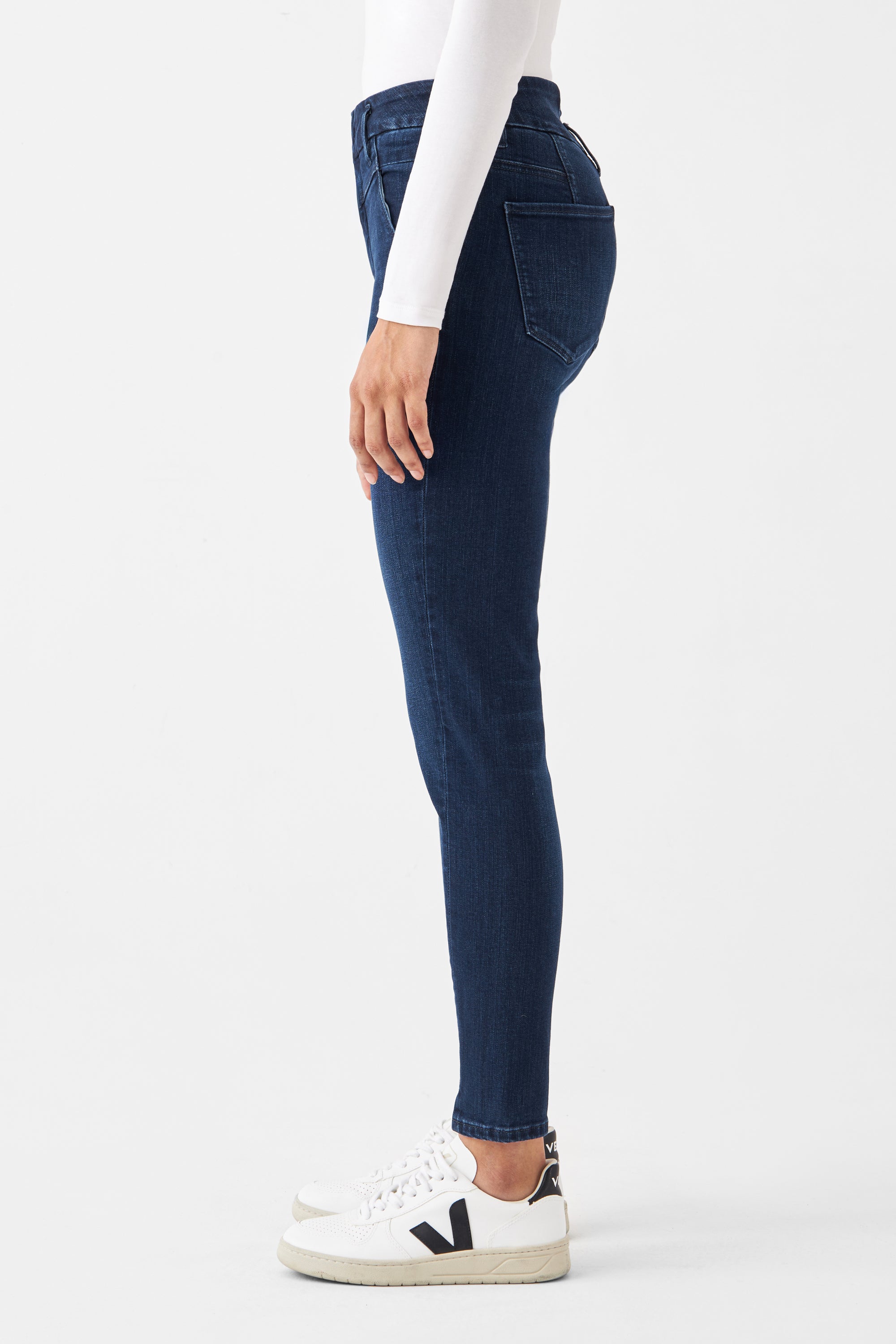 Dunkelblaue SUN UP Skinny Jeans aus Organic Powerstretch, Seitenansicht eines Modells mit engem Bein bis zum Knöchel und weißen Sneakern.