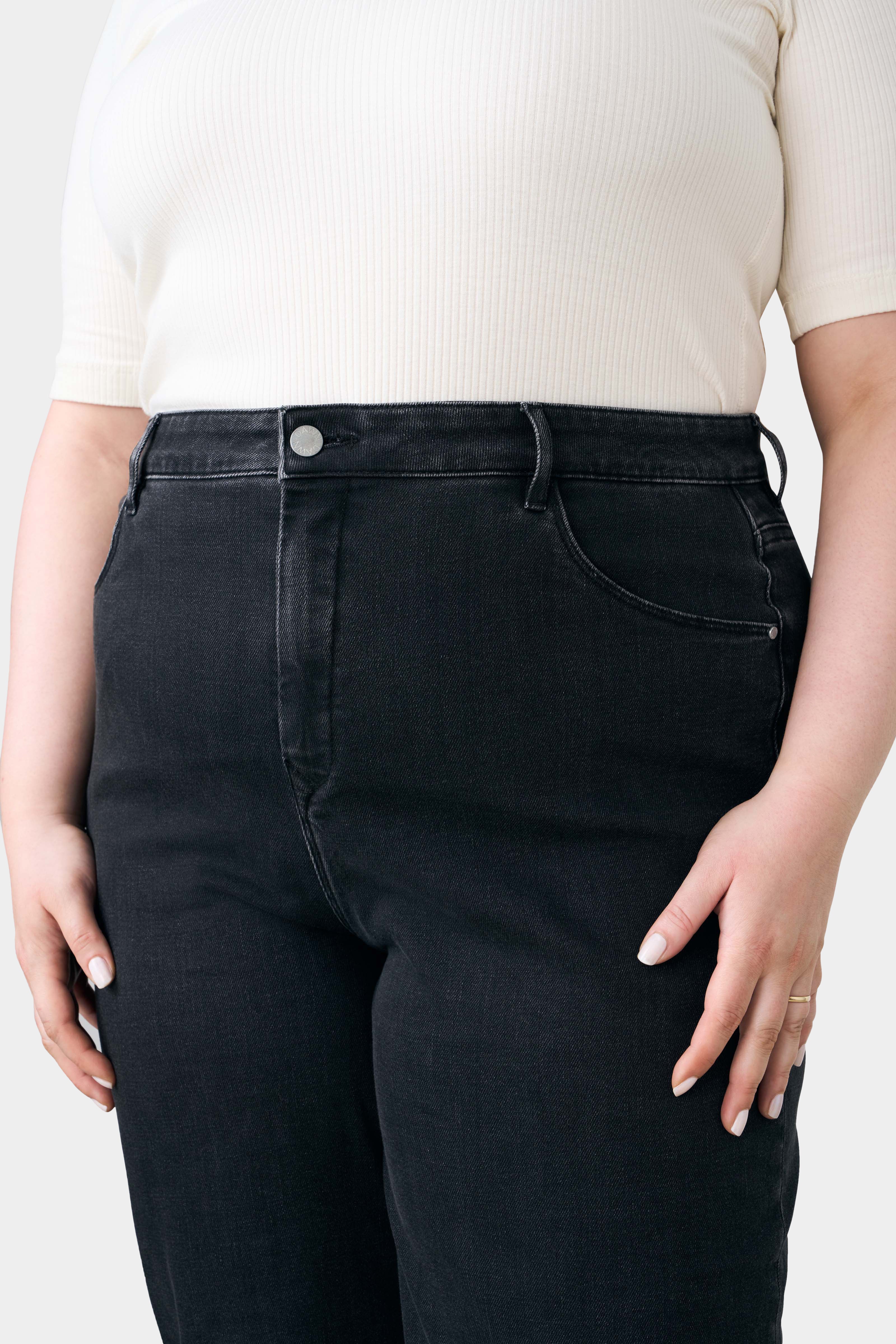 Schwarze DEW Flared Soft Denim-Jeans, High-Waist mit ausgestelltem Bein, klassisches Five-Pocket-Design, zu cremefarbenem Oberteil.