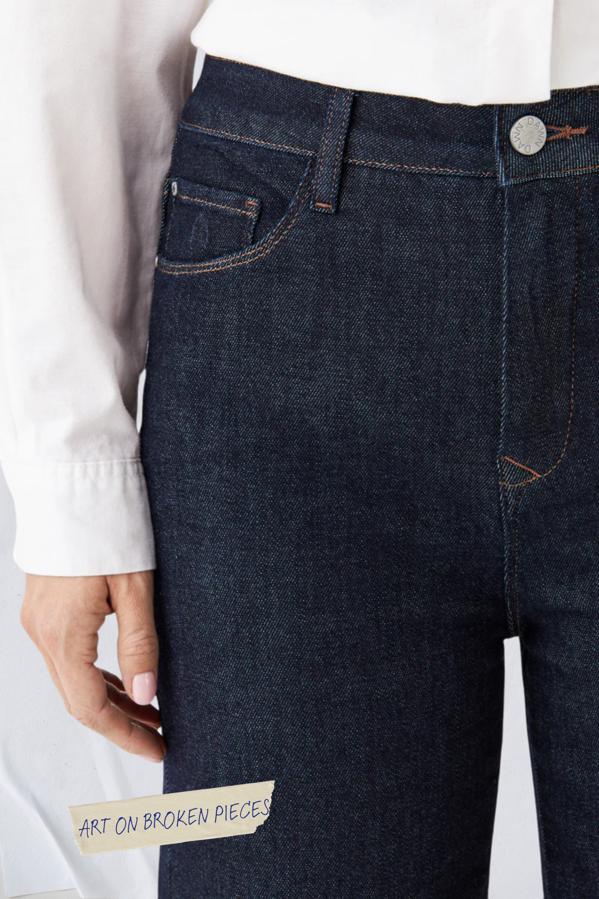 DEW Flared Soft Denim – Classic in Raw Blue, hohe Taille, ausgestelltes Bein; Sticker 'ART ON BROKEN PIECES' am Bein.