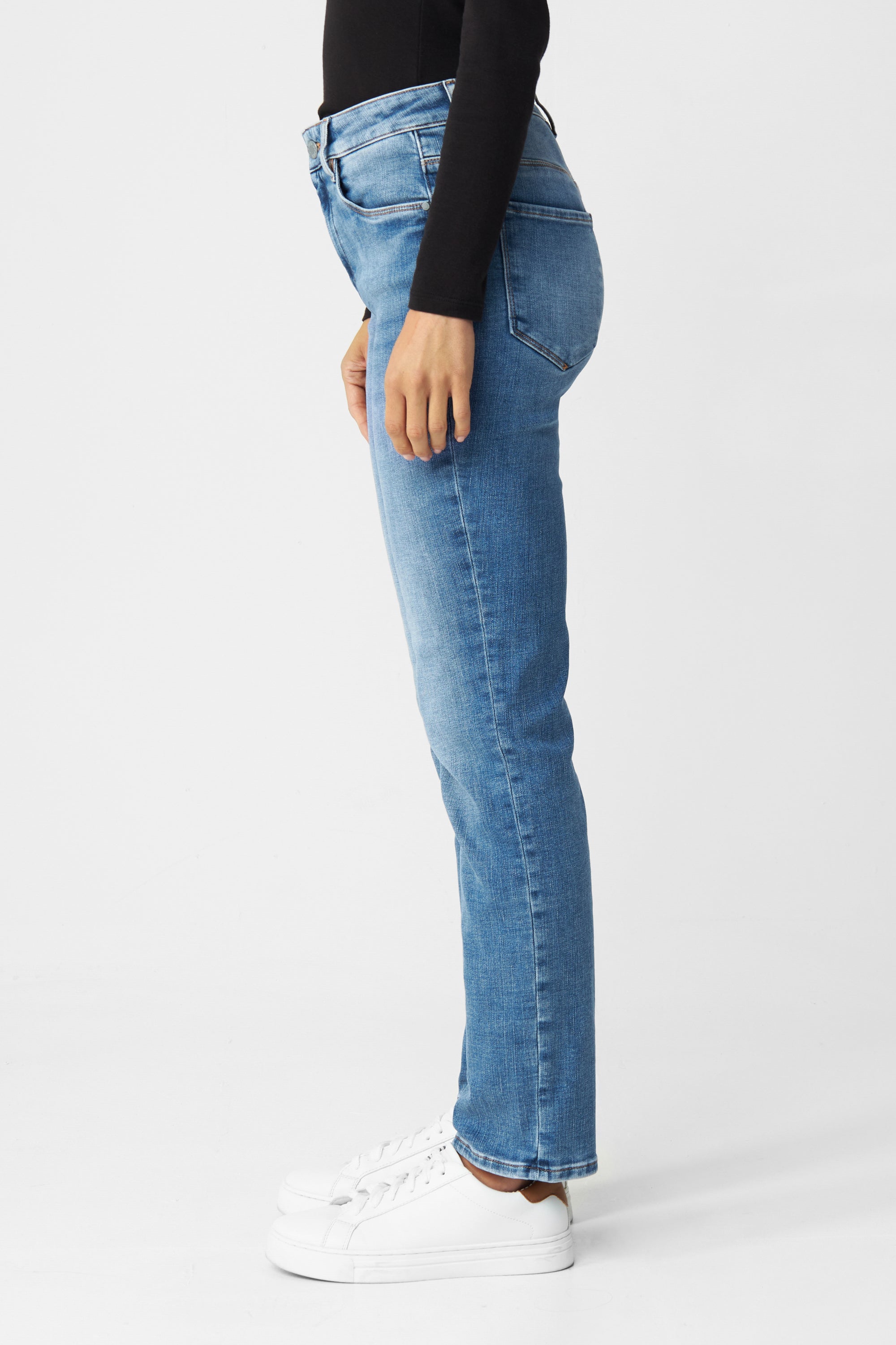 Seitenansicht der STELLAR High-Waist Slim Jeans in Faded Blue, 5-Pocket-Design, schmaler Beinverlauf, mit weißen Sneakern.