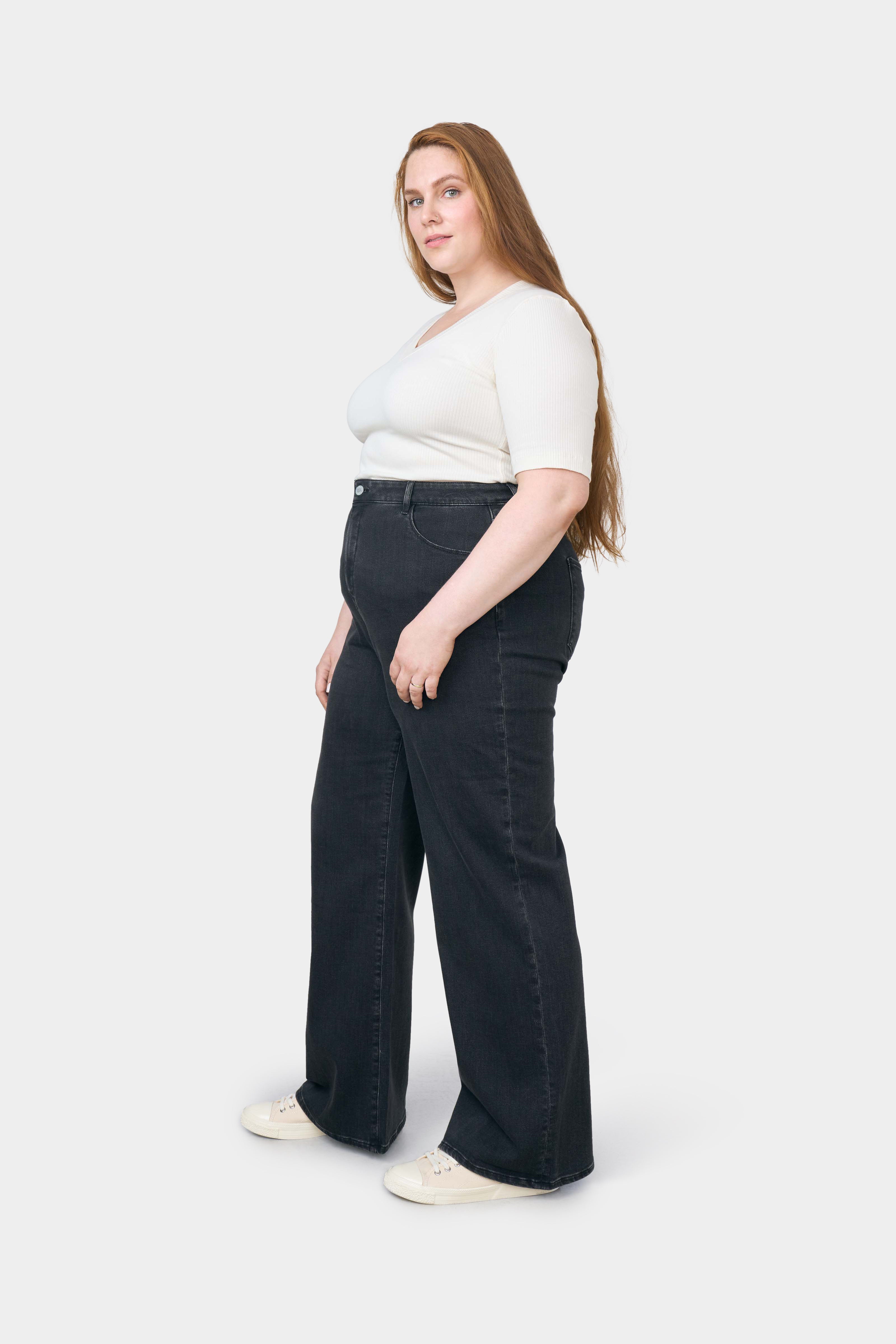 Schwarze High-Waist Flare-Jeans von DEW mit Stretch, an einer Plus-Size-Frau in seitlicher Pose getragen, weißes Top.